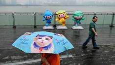 Seorang pejalan kaki menggunakan payung saat melintas di pedestrian Sungai Qiantang. Hangzhou, Zhejiang, China yang berhias maskot Asian Games 2022 (Chenchen, Congcong, dan Lianlian) pada 22 September 2023 waktu setempat. (AFP/Manan Vatsyayana)