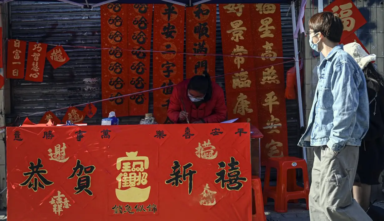 Seorang kaligrafer menulis kuplet musim semi, semacam dekorasi Tahun Baru Imlek, jelang dimulainya Tahun Baru Imlek di sebuah kios di Foshan, Provinsi Guangdong, China, 18 Januari. Kuplet musim semi berasal dari era Shu (lebih dari seribu tahun yang lalu). (Giok Gao/AFP)