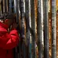 Seorang warga Meksiko terbujur kaku sambil memegang pagar perbatasan sambil berbincang dengan keluarganya di Playas Tijuana, Meksiko, (12/4). Tembok ini memisahkan antara Meksiko dan Amerika Serikat. (REUTERS / Jorge Duenes)