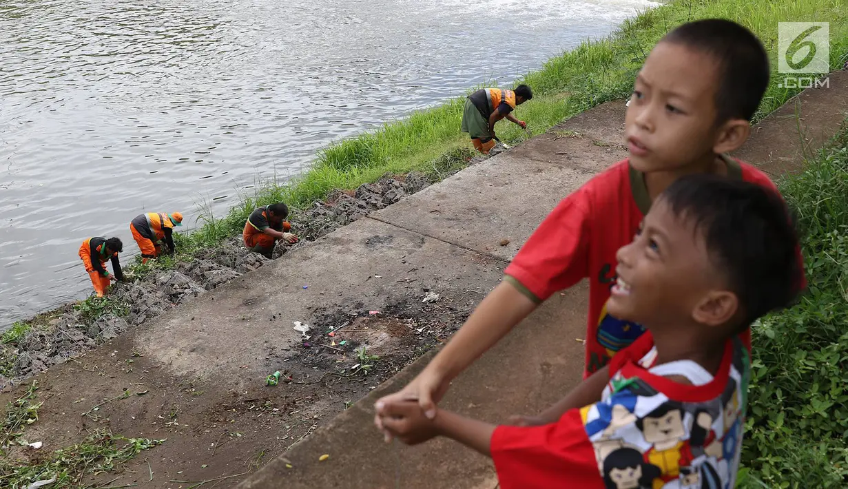 Anak-anak bermain saat sejumlah petugas membersihkan bantaran Kanal Banjir Timur (KBT), Jakarta, Selasa (12/3). Tidak adanya mesin pemotong rumput menyebabkan para petugas melakukan perawatan rutin dengan alat seadanya. (Liputan6.com/Immanuel Antonius)