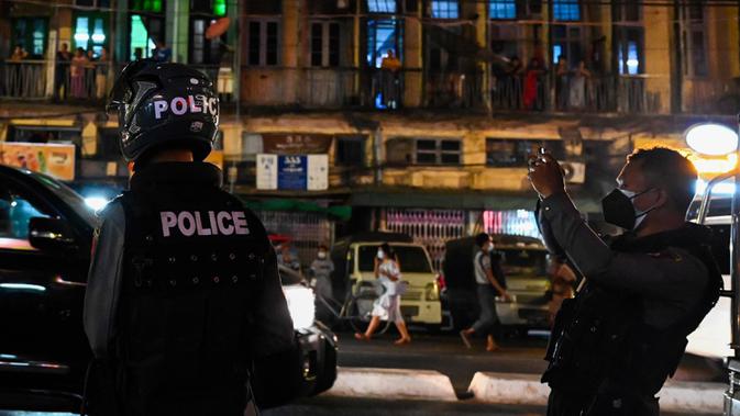 Polisi merekam dengan ponsel saat orang-orang membuat keributan setelah seruan untuk protes keluar di media sosial di Yangon, Myanmar, 3 Februari 2021. Kudeta militer Myanmar terus memicu protes warga dengan membunyikan klakson mobil, menyalakan lampu ponsel, dan memukul-mukul panci. (STR/AFP)