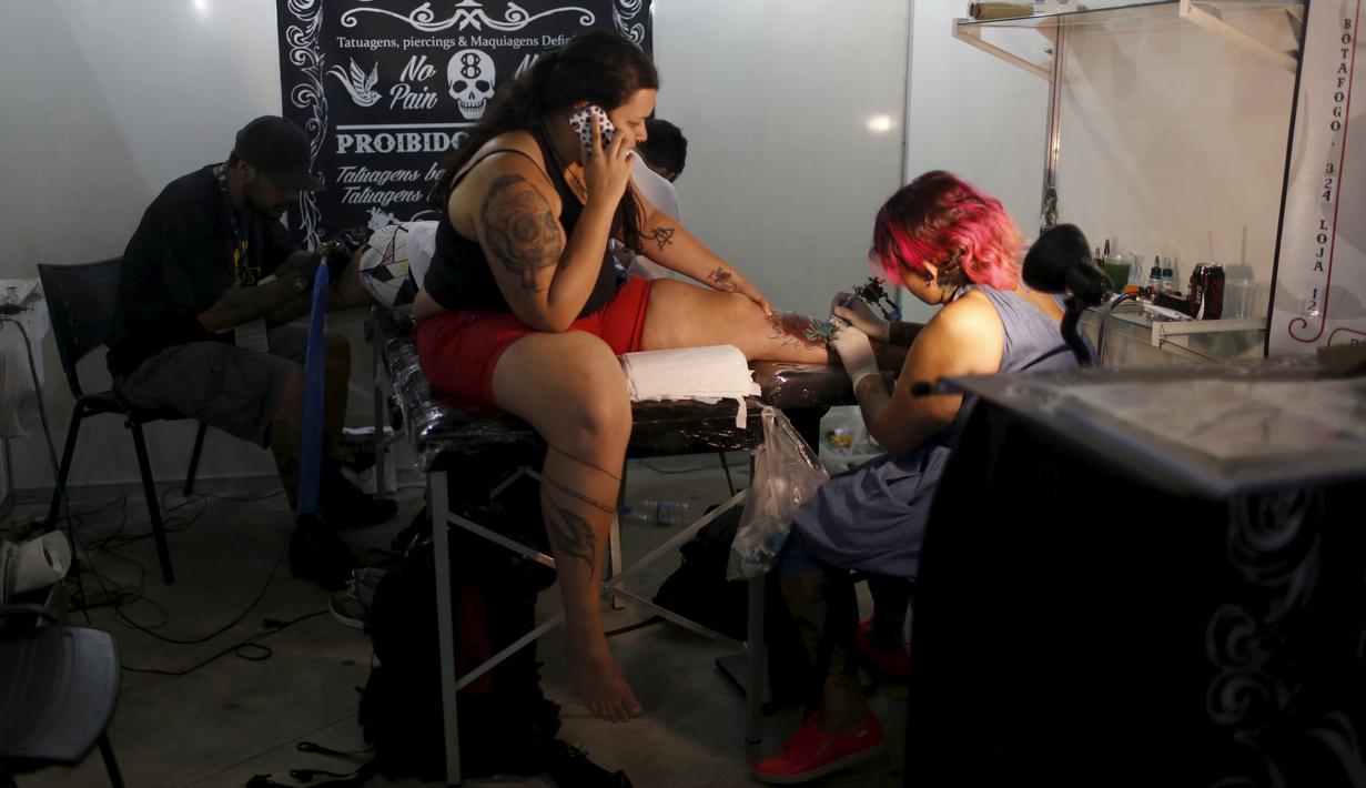 Seorang seniman terlihat serius menato seorang wanita dibagian kakinya saat Festival Internasional Tattoo Week Rio 2016 ketiga di Rio de Janeiro, Brasil, (22/1/2016). (REUTERS/Pilar Olivares)