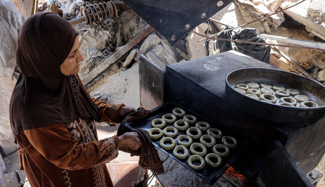 Kaak diisi dengan pasta kurma yang dihaluskan bersama mentega. Tampak dalam foto, seorang wanita bersiap memanggang biskuit tradisional "kaak" yang berbentuk cincin menjelang Idul Fitri, hari raya yang menandai berakhirnya bulan puasa suci Ramadan, di Kota Gaza pada 16 Maret 2026. (Omar AL-QATTAA/AFP)