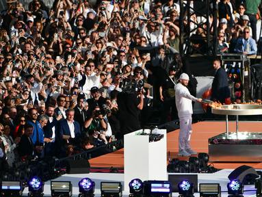 Rapper Prancis, Julien Mari alias Jul lights menyalakan api di kuali relai obor saat upacara penyambutan kedatangan api Olimpiade dan Paralimpiade Paris 2024 di Vieux-Port (Pelabuhan Tua) Marseille, Pranci, Rabu (08/05/2024) waktu setempat. (AFP/Christophe Simon)