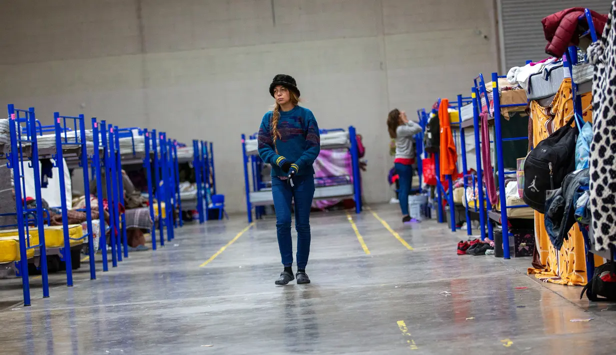 Seorang imigran berjalan di antara deretan tempat tidur susun di tempat penampungan yang dikelola pemerintah di Ciudad Juarez, Meksiko, 18 Desember 2022. Kota-kota perbatasan Texas bersiap menghadapi lonjakan sebanyak 5.000 imigran baru setiap hari yang melintasi perbatasan AS-Meksiko karena pembatasan imigrasi era pandemi berakhir minggu ini. (AP Photo/Andres Leighton)