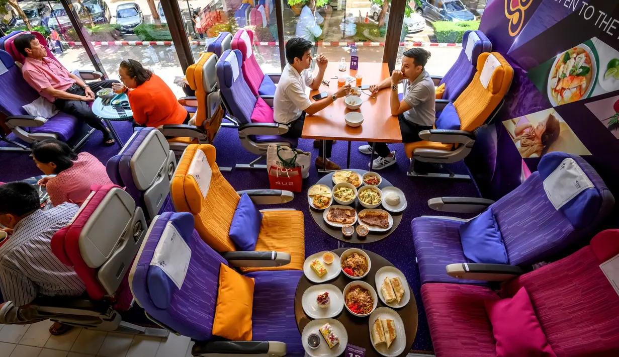 Orang-orang duduk di kursi pesawat saat makan di restoran pop-up bertema kabin pesawat di kantor pusat Thai Airways di Bangkok, 10 September 2020. Restoran pop-up ini menyajikan sekitar 2.000 makanan per hari untuk memulihkan pendapatan yang hilang selama pandemi virus corona. (Mladen ANTONOV/AFP)