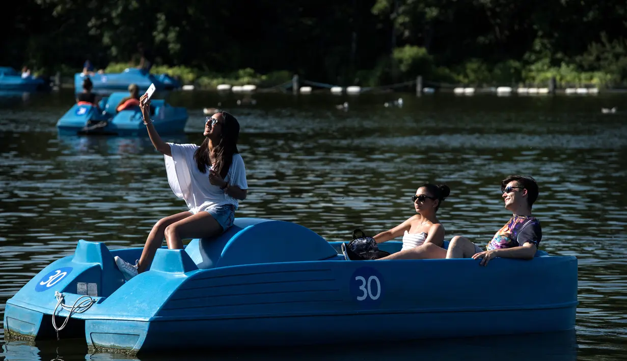 Warga berada di perahu menikmati hangatnya cuaca di dekat Serpentine di Hyde Park di London, Inggris (5/7). Sinar matahari yang hangat dimanfaatkan warga Inggris untuk berjemur dan bersantai dengan keluarga atau teman. (AFP Photo/Niklas Hallen)