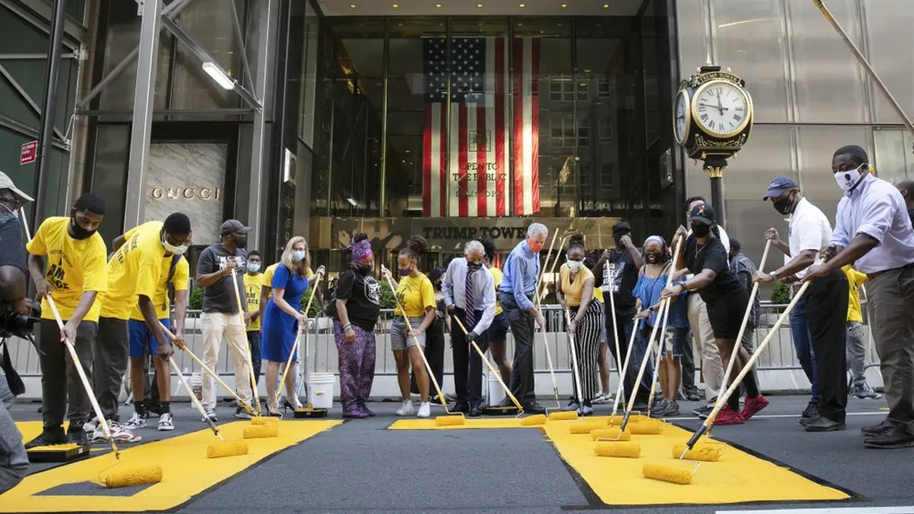 Walikota New York, Bill de Blasio, yang mengenakan masker oranye, berpartisipasi dalam melukis mural Black Lives Matter di Fifth Avenue di depan Trump Tower, New York, AS Kamis (9/7/2020) (Photo Credit: AP/Mark Lennihan)
