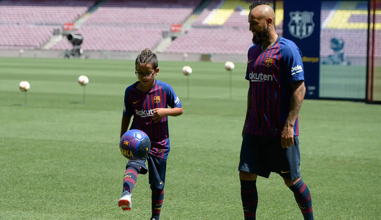 Pemain baru Barcelona, Arturo Vidal melihat putranya Alonso Vidal menunjukkan skill bermain bola selama presentasi dirinya di stadion Camp Nou, Spanyol, (6/8). (AFP Photo/Josep Lago)