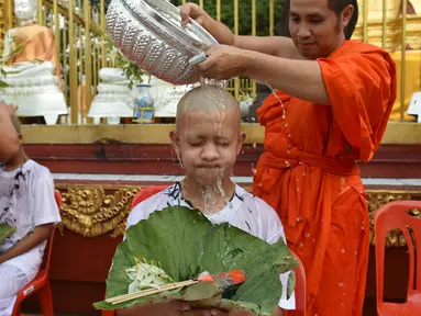 Biksu mengguyur kepala salah satu anak, yang diselamatkan dari gua di Thailand, pada upacara pentahbisan di Kuil Wat Phra That Doi Wao, Chiang Rai, Selasa (24/7). Sebanyak 11 remaja menjalani ritual menjadi biksu. (Panumas Sanguanwong/THAI NEWS PIX/AFP)