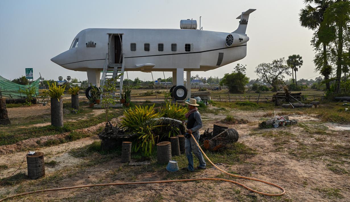 Foto yang diambil pada 12 Maret 2023 ini memperlihatkan Chrach Peou sedang menyemprotkan air di taman depan rumahnya yang berbentuk pesawat terbang di provinsi Siem Reap, Kamboja. (Photo by TANG CHHIN SOTHY / AFP)