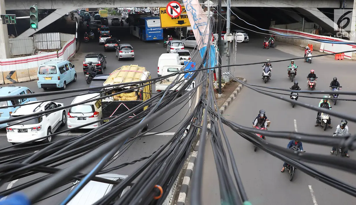 Kendaraan melintas di bawah Instalasi kabel menjuntai di Jalan Dewi Sartika, Jakarta Timur, Sabtu (19/1). Selain mengganggu keindahan kota, kondisi tersebut juga berbahaya karena dapat memicu hubungan pendek arus listrik. (Liputan6.com/Immanuel Antonius)