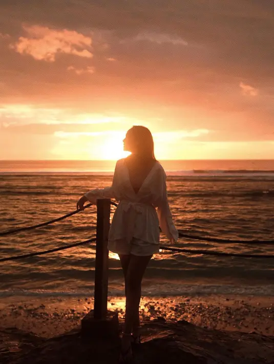 Kali ini, terlihat sedang menikmati momen matahari terbenam, siluet dirinya tampak mengenakan setelan robe putih dan celana pendek berpose di pinggir pantai. Foto: Instagram.