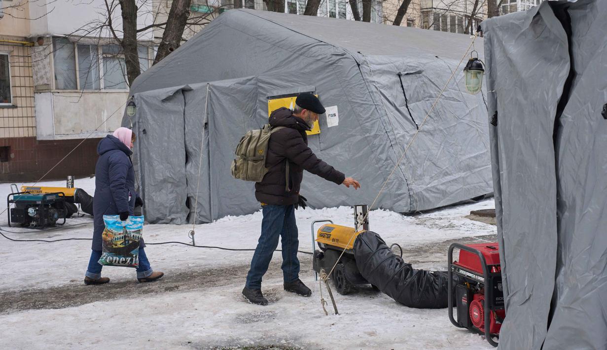 Kerusakan parah pada jaringan distribusi diperparah oleh lonjakan penggunaan pemanas listrik oleh warga yang berupaya melawan dingin ekstrem. Tampak dalam foto, seorang pria menghangatkan diri di tenda-tenda darurat tempat orang-orang dapat menghangatkan diri setelah serangan udara rutin Rusia terhadap fasilitas energi negara itu di tengah musim dingin, Kyiv, Ukraina, Selasa 13 Januari 2026. (AP Photo/Efrem Lukatsky)