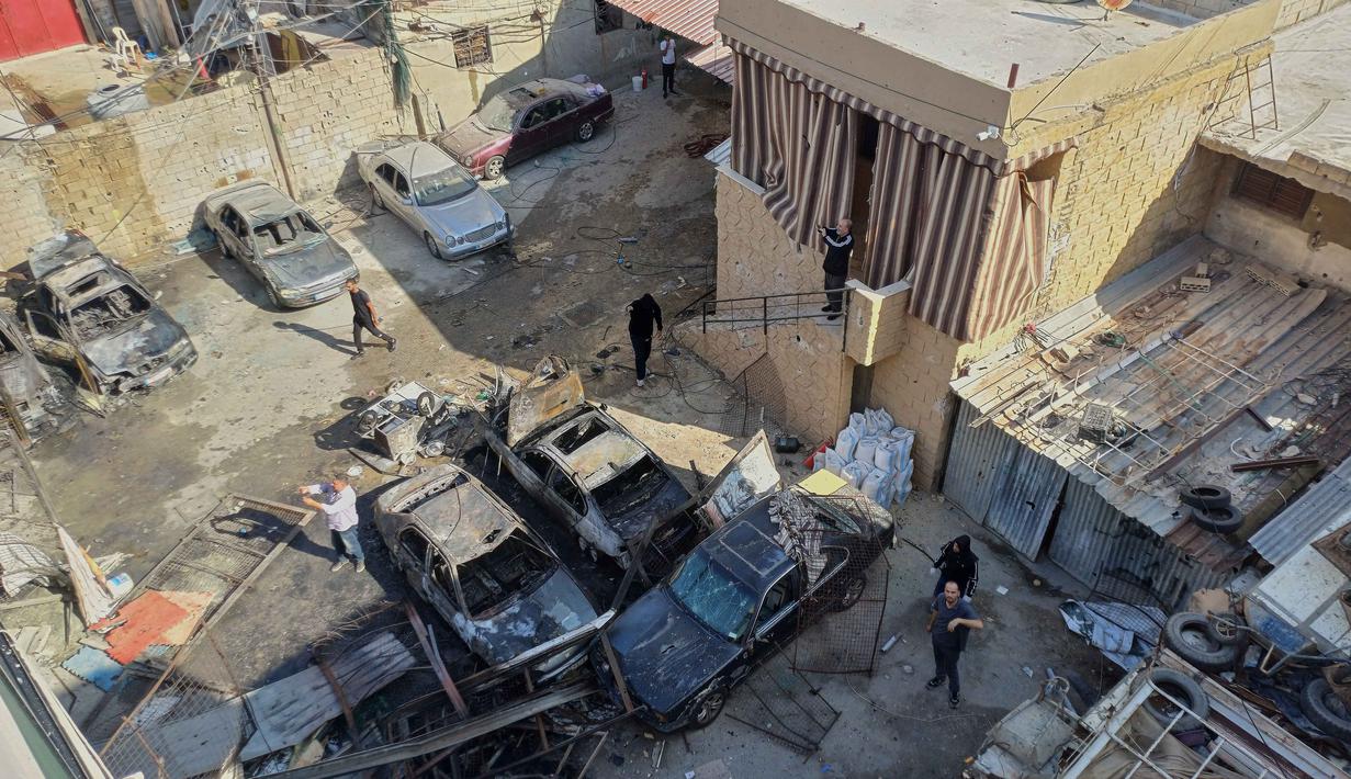 Serangan terjadi pada Selasa 18 November 2025 malam waktu setempat. Tampak dalam foto, warga berkumpul di sekitar mobil-mobil yang rusak akibat serangan Israel pada Selasa malam di kamp pengungsi Palestina Ein el-Hilweh, di kota pelabuhan selatan Sidon, Lebanon, Rabu 19 November 2025. (AP Photo/Mohammed Zaatari)