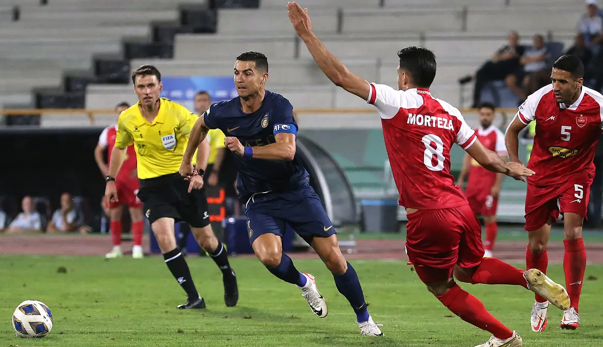 Pemain Al-Nassr, Cristiano Ronaldo (tengah) berusaha melewati pemain Persepolis, Morteza Pouraliganji pada laga Grup E Liga Champions Asia 2023/2024 di Azadi stadium, Teheran, Iran, 19 September 2023. (AFP/Atta Kenare)