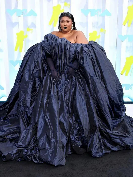 Penyanyi Lizzo memilih tampilan dramatis untuk karpet merah MTV VMA 2022 dengan gaun Jean Paul Gaultier Couture yang menakjubkan. Gaun biru tua menampilkan kain yang mengepul dalam gelombang, hampir seperti air terjun. Penampilannya itu dipadukan dengan lipstik warna senada. (twitter/lizo).