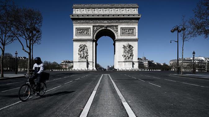 Seorang pria mengendarai sepedanya melewati Arc de Triumph selama kebijakan lockdown berlangsung untuk menghentikan penyebaran pandemi virus corona Covid-19 di Paris pada 23 Maret 2020. (Photo by PHILIPPE LOPEZ / AFP)
