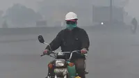 Pengendara motor mengenakan masker saat kabut asap tebal di Lahore (21/11/2019). Akibat kabut asap tebal penduduk Lahore mengeluh sakit tenggorokan, mata gatal dan penyakit lainnya.  (AFP Photo/Arif Ali)