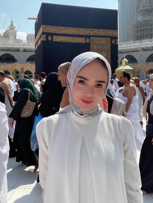 Yuni Shara saat berpose di depan Kakbah. Dia mengenakan gamis putih yang dipadukan dengan hijab bercorak. (Foto: Instagram/ yunishara36)
