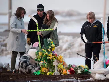 Sebuah keluarga menempatkan salib yang terbuat dari tongkat hoki untuk memberi penghormatan kepada korban kecelakaan bus yang membawa tim hoki es Humboldt Broncos di Provinsi Saskatchewan, Kanada (9/4). (Jonathan Hayward/The Canadian Press via AP)