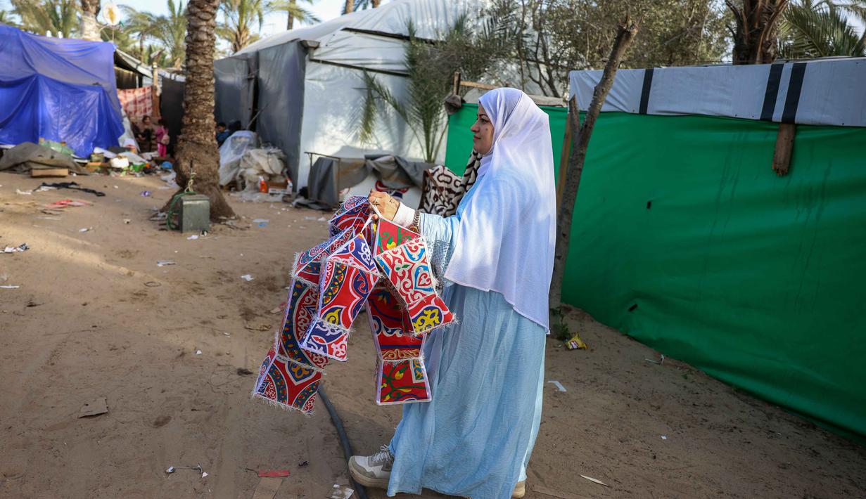 Bagi Rehan Hazem Sharab, fanous, selain membawa kegembiraan ke tenda-tenda dan reruntuhan rumah yang hancur, sekaligus sumber penghasilan untuk menghidupi kedua anaknya dengan menjual lampion tersebut ke toko-toko. Tampak dalam foto, Rehan Hazem Sharab, seorang pengungsi Palestina berusia 32 tahun, memegang lampion buatan tangannya yang terbuat dari kotak-kotak bantuan bekas sebagai persiapan menyambut bulan suci Ramadan yang dimulai pada 17 Februari, di luar tendanya di lingkungan Al-Mawasi, Khan Younis, di Jalur Gaza selatan pada Sabtu 7 Februari 2026. (Bashar Taleb/AFP)