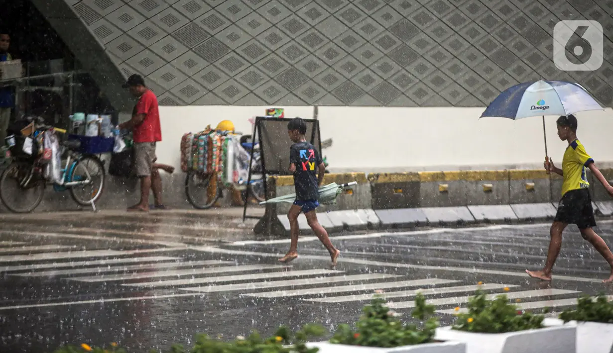 Anak-anak yang bekerja sebagai ojek payung menyeberang jalan saat hujan deras di kawasan Thamrin, Jakarta, Rabu (23/11/2022). Sejak Oktober, DKI Jakarta mulai memasuki musim penghujan yang sudah masuk ke dalam tahap ekstrem. (Liputan6.com/Faizal Fanani)