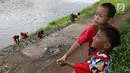 Anak-anak bermain saat sejumlah petugas membersihkan bantaran Kanal Banjir Timur (KBT), Jakarta, Selasa (12/3). Tidak adanya mesin pemotong rumput menyebabkan para petugas melakukan perawatan rutin dengan alat seadanya. (Liputan6.com/Immanuel Antonius)