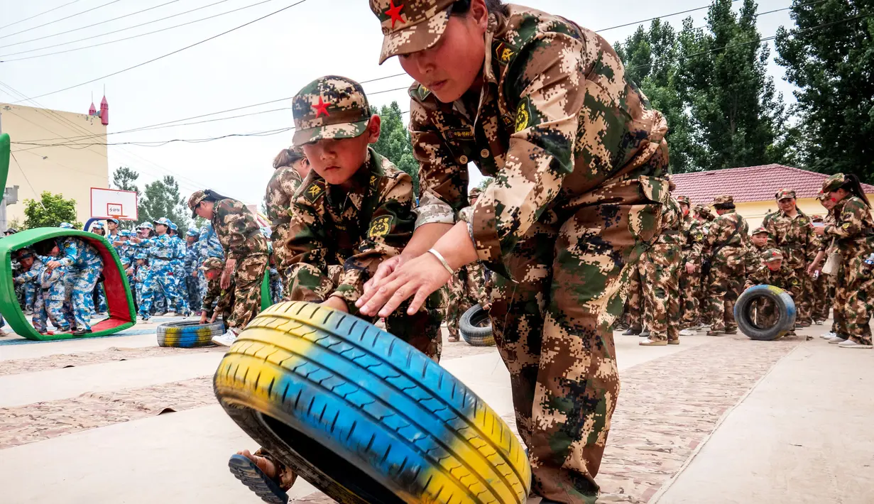 Sejumlah anak-anak mendorong ban saat mensimulasikan latihan militer di sebuah taman kanak-kanak di provinsi Henan, China (30/5). Latihan militer ini dilakukan untuk menjelang Hari Anak Internasional yang jatuh pada 1 Juni. (AFP)