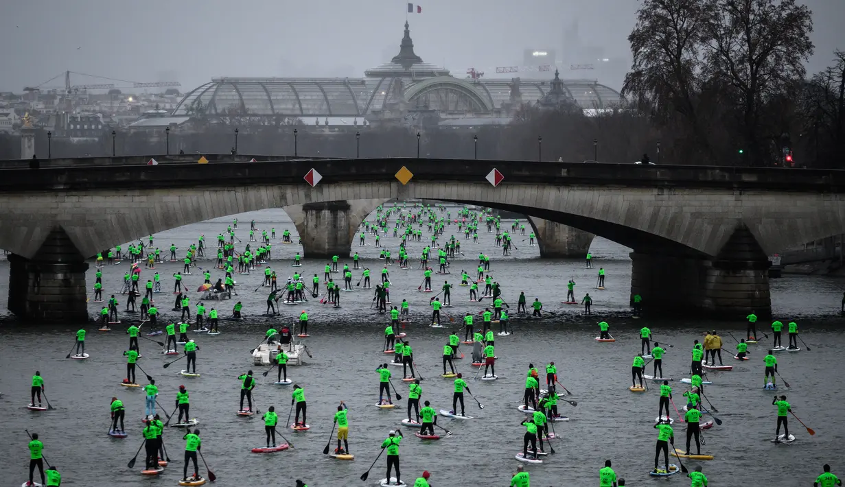 Peserta mengambil bagian dalam Nautic Paddle Race atau lomba dayung sambil berdiri dengan latar belakang The Grand Palais di sungai Seine, Paris, Minggu (8/12/2019). Sekitar 1000 pesaing ikut serta dalam lomba sejauh 11 km menyeberangi sungai Seine. (Photo by Olivier MORIN / AFP)