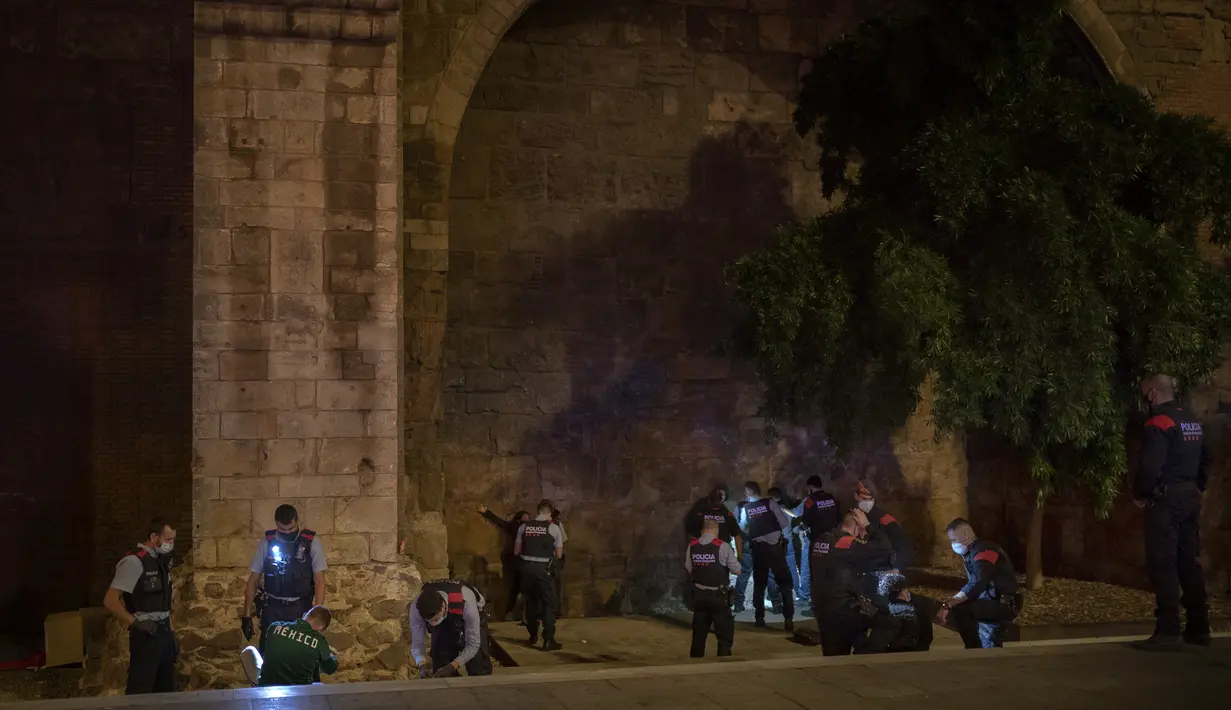Orang-orang ditahan dan diperiksa Mossos d'Escuadra, kepolisian regional Catalonia, setelah jam malam di Barcelona pada 1 November 2020. Pemerintah Spanyol menetapkan pembatasan gerak atau jam malam yang berlaku pukul 22.00 untuk mengendalikan lonjakan kasus Covid-19. (AP Photo/Emilio Morenatti)