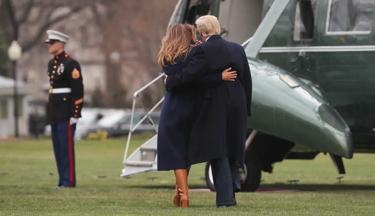 Presiden AS Donald Trump merangkul Melania Trump yang hampir terjatuh saat berjalan menuju helikopter kepresidenan di Gedung Putih, Senin (19/3). Melania Trump kehilangan keseimbangan saat mengenakan sepatu berhak 10 cm itu.  (AP/Pablo Martinez Monsivais)