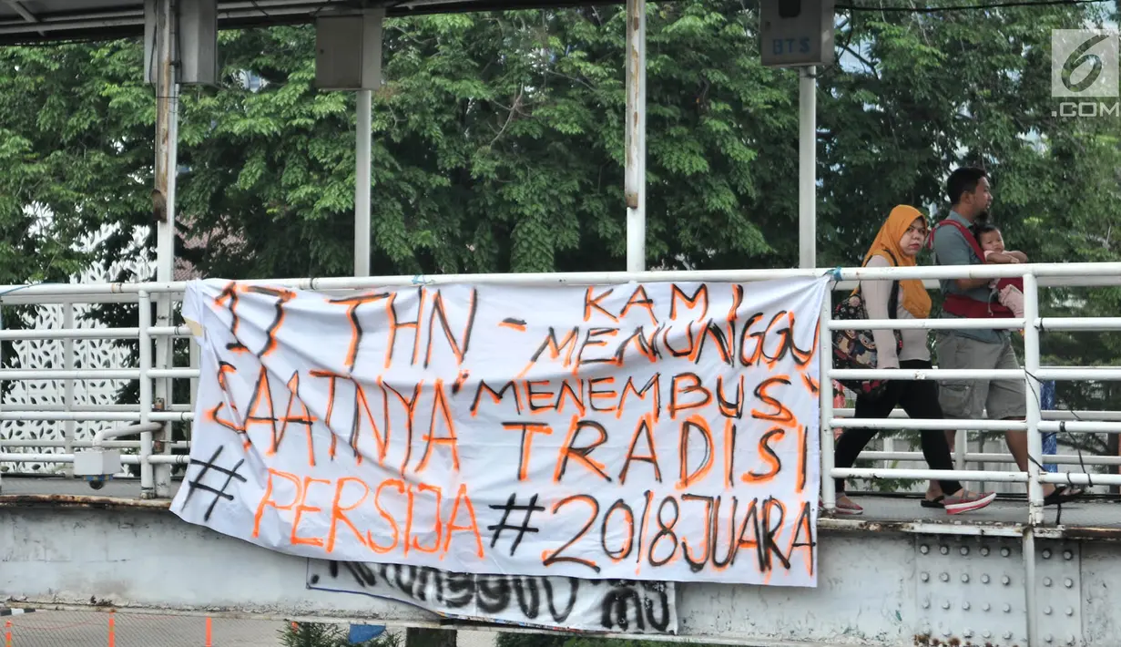 Warga melintasi spanduk dukungan Persija yang terpasang di JPO, Jakarta, Minggu (9/12).  Dalam spanduk tersebut bertuliskan berbagai ungkapan dukungan dan doa para The Jakmania agar Persija menjadi juara Liga 1 2018. (Merdeka.com/Iqbal S. Nugroho)