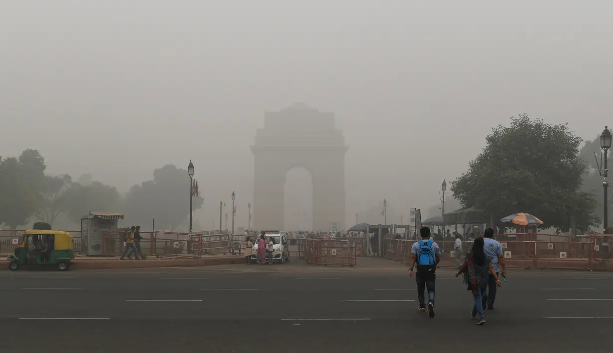 Turis menyebrang jalan untuk mengunjungi India Gate atau Gerbang India yang diselimuti kabut asap pekat di New Delhi, Minggu (3/10/2019). Ibu Kota dari India tersebut sedang dilanda polusi udara yang sangat buruk sekaligus beracun pekan ini. (Photo by Sajjad  HUSSAIN / AFP)