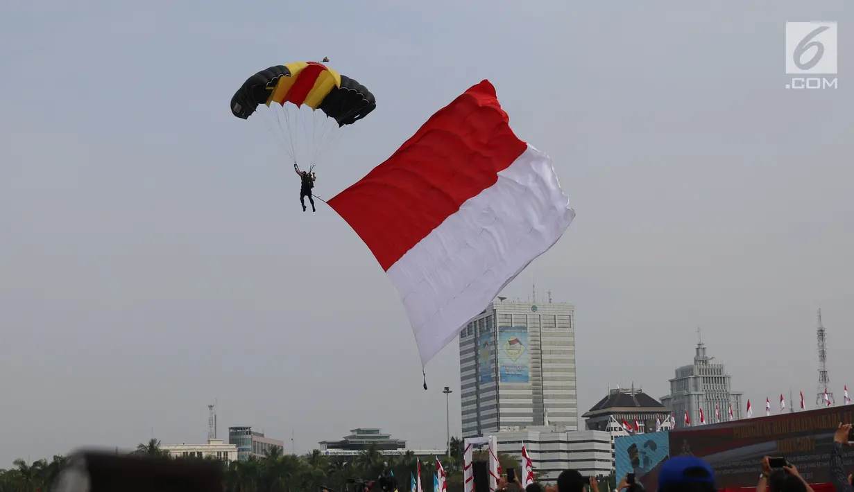 Personel Polri membawa bendera merah putih saat atraksi terjun payung pada peringatan HUT Bhayangkara ke-71 di Silang Monas, Jakarta, Senin (10/7). Acara ini menampilkan berbagai atraksi dari masing-masing kesatuan Polri. (Liputan6.com/Angga Yuniar)