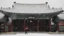 Seorang wanita menggunakan payung  berjalan saat hujan salju di Istana Gyeongbok di Seoul, Korea Selatan (13/12). Istana Gyeongbok merupakan kerajaan utama selama Dinasti Joseon dan salah satu landmark terkenal di kota tersebut. (AFP Photo/Lee Jin-man)