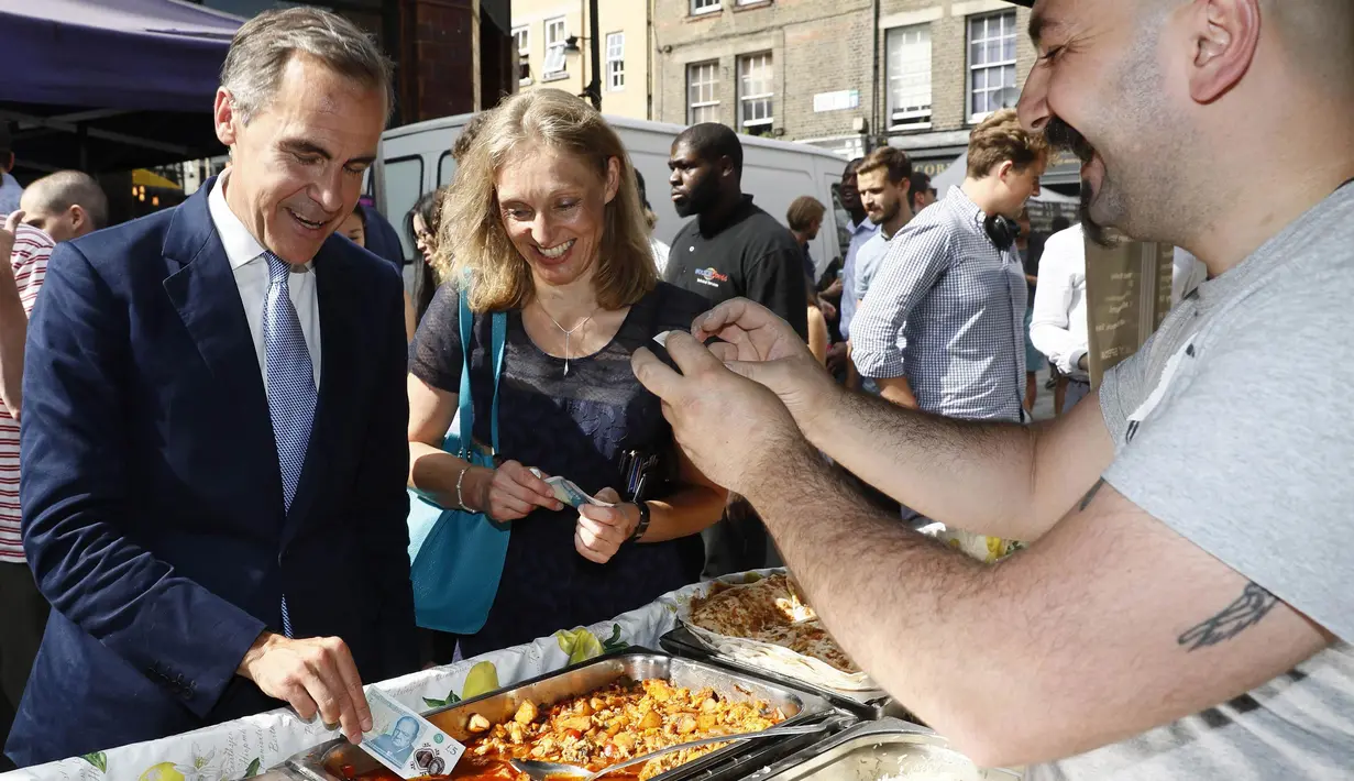 Gubernur Bank Inggris, Carney mengetes uang keluaran baru saat ia membeli makan siang di Whitecross Street Market di London, Selasa (13/9). Uang tersebut terbuat dari plastik film berbahan polimer. (REUTERS / Stefan Wermuth)