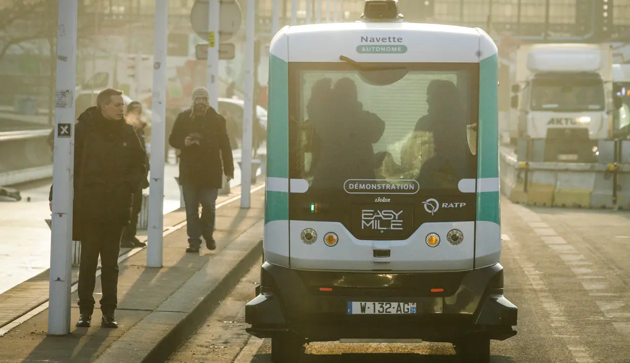 Pejalan kaki mengamati bus listrik swakemudi (otonom) yang memulai uji coba pertama pengoperasian antara stasiun Austrelitz dan stasiun Lyon, Paris, Senin (23/1). Kendaraan berbentuk kotak itu mampu membawa sekitar 10 orang. (GEOFFROY VAN DER HASSELT/AFP)