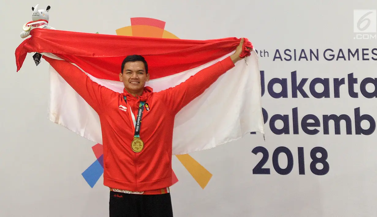 Pesilat Indonesia, Aji Bangkit Pamungkas mengibarkan bendera Merah Putih usai meraih medali emas ke-16 untuk Indonesia dalam babak final Kelas I Putra Asian Games 2018 di TMII, Jakarta, Senin (27/8). (Merdeka.com/Arie Basuki)