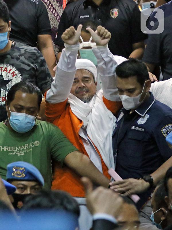 M Rizieq Shihab (tengah) digiring petugas saat meninggalkan gedung Ditreskrimum Polda Metro Jaya, Jakarta, Minggu dini hari (13/12/2020). Rizieq Shihab ditahan setelah menjalani pemeriksaan sebagai tersangka penghasutan dan kerumunan di tengah pandemi COVID-19. (Liputan6.com/Helmi Fithriansyah)