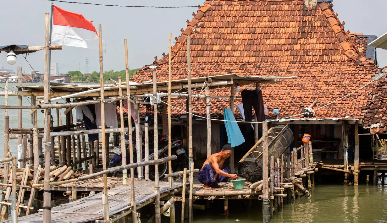Situasi ini sudah terjadi sejak 2014, wilayah yang dulunya pemukiman dan sawah kini berubah total menjadi perairan. Tampak dalam foto, seorang pria bekerja di luar rumah yang sebagian terendam air laut akibat banjir pasang di desa Timbulsloko, Demak, Jawa Tengah pada Sabtu 18 April 2026. (DEVI RAHMAN/AFP)