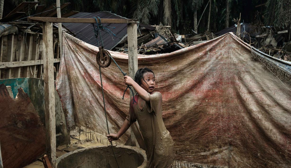 Akses makan yang terbatas sampai kebersihan yang sulit dijaga bisa memengaruhi kondisi fisik dan kesehatan anak. Tampak dalam foto, Baiti Arafah mengambil seember air dari sumur untuk membersihkan diri setelah bermain di genangan lumpur di Babo, Aceh Tamiang, pada Senin 15 Desember 2025. (Yasuyoshi Chiba/AFP)
