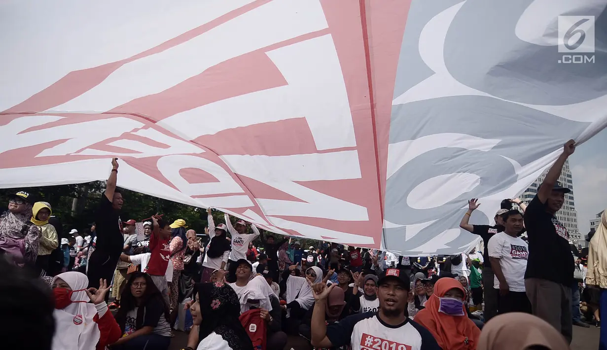 Massa berteduh di bawah bendera raksasa bertuliskan '#2019GantiPresiden' saat deklarasi akbar di Monas, Jakarta, Minggu (6/5). Acara ini juga diramaikan dengan penjualan kaus dan atribut bertagline #2019GantiPresiden. (Merdeka.com/Iqbal Nugroho)