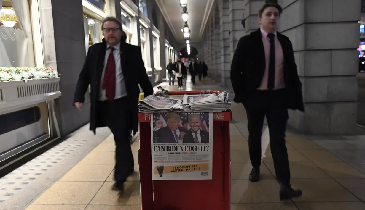 Orang-orang berjalan melewati tumpukan surat kabar Evening Standard yang menampilkan gambar kandidat presiden AS, Presiden Donald Trump dan kandidat Demokrat Joe Biden, di London, Inggris pada Rabu (4/11/2020). (AP Photo/Alberto Pezzali)