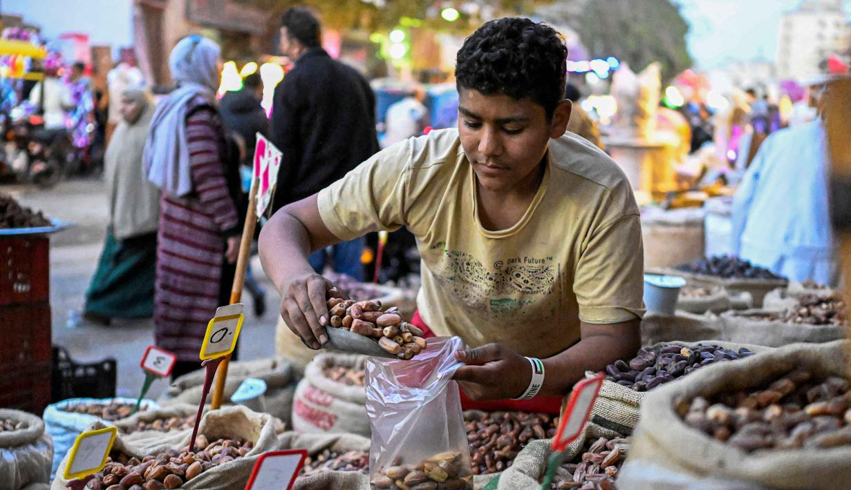 Selain berpuasa, bagi umat muslim, Ramadan merupakan waktu yang tepat untuk melakukan refleksi spiritual, meningkatkan doa, serta berkumpul bersama keluarga. Tampak dalam foto, seorang pedagang Mesir mengisi kurma untuk seorang pelanggan di pasar, distrik Sayyida Zeinab, pusat kota Kairo, pada Kamis 12 Februari 2026. (Khaled DESOUKI/AFP)