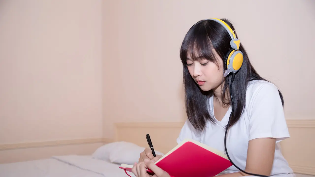 Seorang Wanita Sedang Mencatat Sambil Mendengarkan Musik