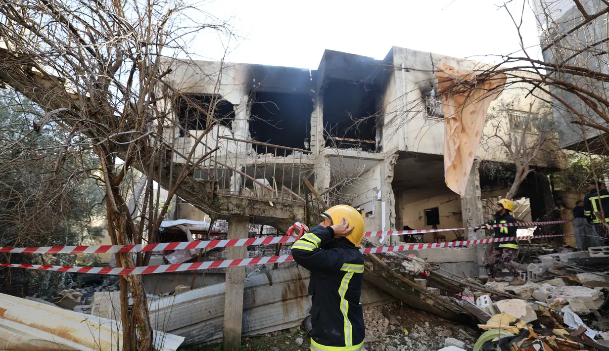 Petugas berada di depan sebuah bangunan yang rusak dan dibakar oleh pasukan Israel selama penggerebekan di kamp pengungsi Jenin Tepi Barat, pada 26 Januari 2023. Serangan Israel di kamp pengungsi Jenin hari ini menewaskan 9 warga Palestina termasuk seorang wanita lanjut usia, kata pejabat Palestina. (AFP/Jaafar Ashtiyeh)