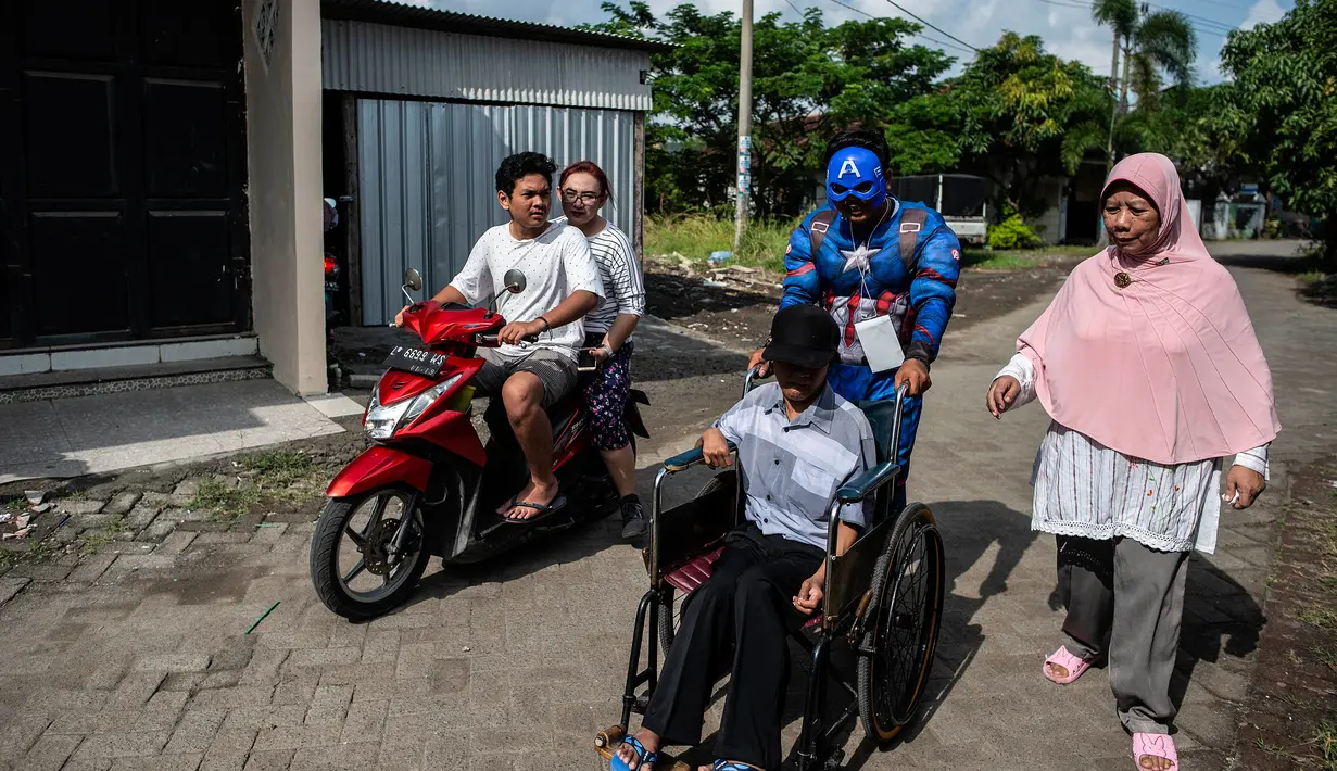 Petugas Kelompok Penyelenggara Pemungutan Suara (KPPS) berkostum superhero Captain America membantu warga berkursi roda yang akan mencoblos dalam Pemilu 2019 di sebuah TPS di Surabaya, Jawa Timur, Rabu (17/4). (Juni Kriswanto/AFP)