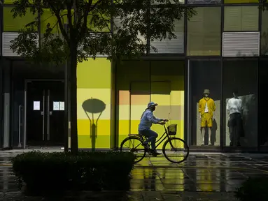 Seorang perempuan mengenakan masker mengendarai sepeda melewati toko-toko yang tutup untuk pengendalian COVID-19 di sebuah pusat perbelanjaan di Beijing, China, Selasa (17/5/2022). Pada Minggu (15/5) kemarin, Beijing memperpanjang aturan untuk bekerja dari rumah di empat distrik. Itu sudah melarang layanan makan di restoran dan membatasi transportasi umum, di antara langkah-langkah lainnya. (AP Photo/Mark Schiefelbein)