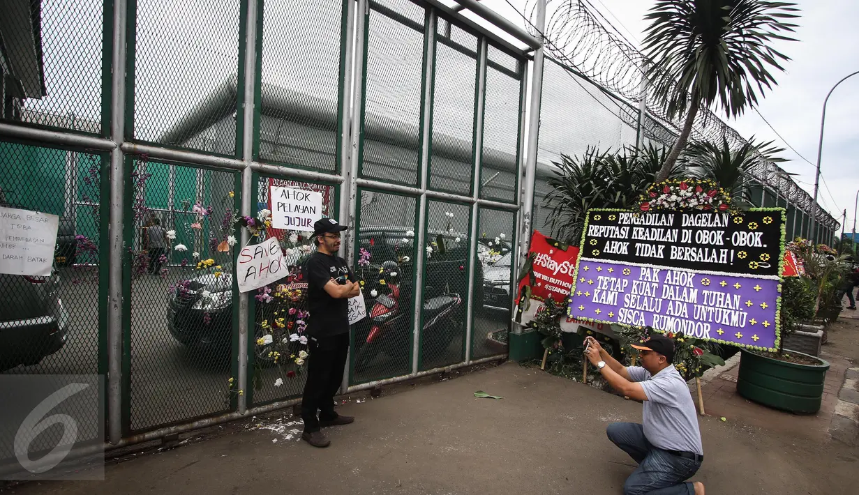 Warga berfoto di antara poster dan karangan bunga dukungan untuk Basuki Tjahaja Purnama (Ahok) di depan Rutan Cipinang, Jakarta, Rabu (10/5). Karangan bunga terus berdatangan, meski Ahok sudah dipindahkan ke Rutan Mako Brimob. (Liputan6.com/Faizal Fanani)